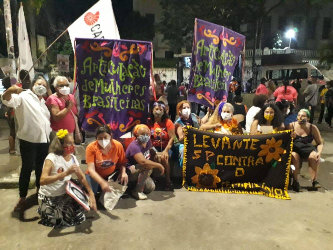 Integrantes da AMB São Paulo, em manifestação do 8 de Março. Elas seguram enormes estandartes da Articulação de Mulheres Brasileiras e uma faixa com fundo preto, escrito em amarelo: Levantes SP contra o feminicídio.